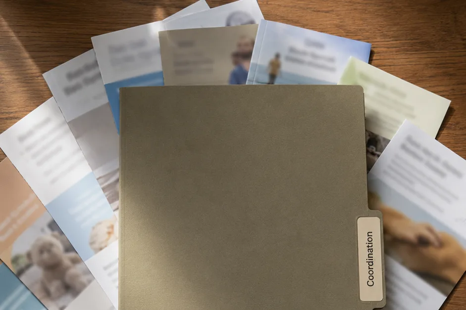 A single quality folder labeled Coordination resting on a fanned-out stack of thin generic benefit flyers.