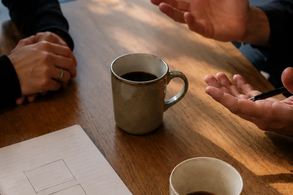 Three coffee cups arranged on a wood table at a small meeting with a notepad showing three rough boxes